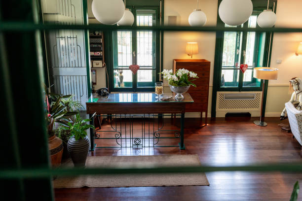 Elegant interior view through windowpanes, highlighting a classic wooden table with floral arrangement, flanked by verdant plants and ambient lighting, in a charming boutique hotel's living space.