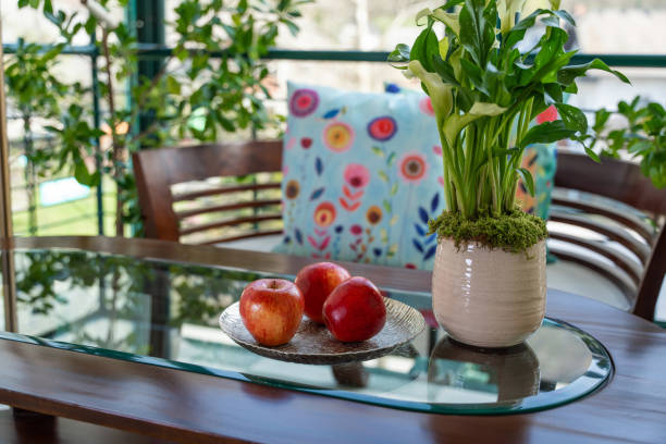 Elegant table setting in a vintage boutique hotel, featuring a glass tabletop with fresh apples, a floral vase, and chic furniture in a serene environment.