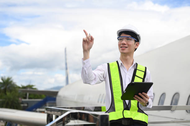 Young aviation engineer with digital tablet standing on a metal railing next to an airplane