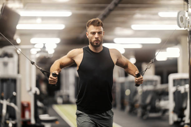 istock Front view of muscular sportsman practicing his biceps and shoulders on exercise machine in gym. 2167352200