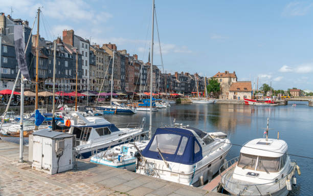 Honfleur, Normandy, France - May 30, 2025: Honfleur Vieux Bassin harbor with boats and yachts moored in the still water, and a row of colorful buildings in the background