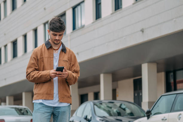 istock Casual young man walking through the city while looking at mobile phone 2167355593