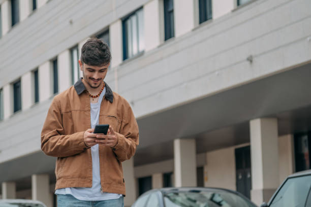 istock Casual young man walking through the city while looking at mobile phone 2167355595