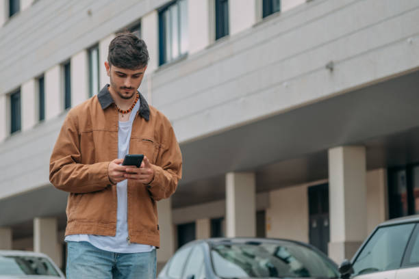 istock Casual young man walking through the city while looking at mobile phone 2167355597