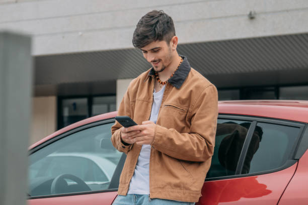 istock Casual young man leaning on car using mobile phone 2167355629