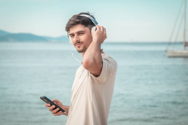 istock young man on beach with back turned wearing headphones... 2167355663