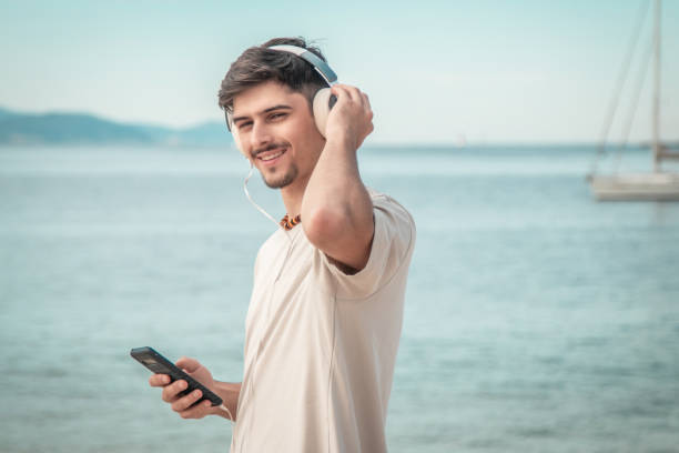 istock young man on beach with back turned wearing headphones... 2167355672