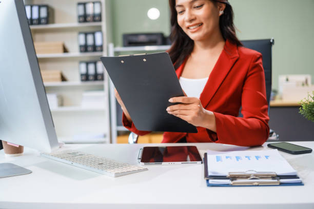 istock An Asian businesswoman sits at her desk, working efficiently on a computer and tablet. She smiles confidently, displaying her expertise as a financial analyst. Her work brings her happiness 2167359880