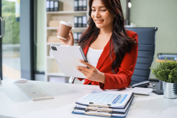 istock An Asian businesswoman sits at her desk, working efficiently on a computer and tablet. She smiles confidently, displaying her expertise as a financial analyst. Her work brings her happiness 2167360374