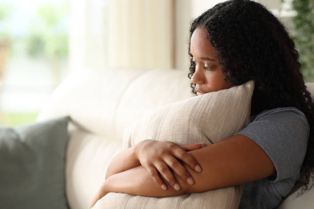 istock Sad black woman embracing pillow on a couch at home 2167367385
