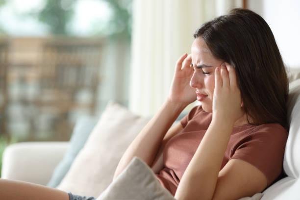 Woman suffering migraine and complaining sitting on a couch at home stock photo