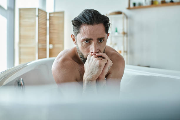 A thoughtful man reflects on his emotions while sitting in a bathtub at home