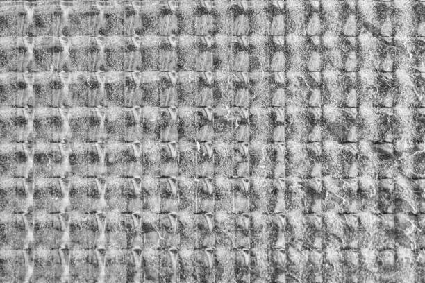 Close-up of a glass window with a textured pattern. The glass has a checkered design, with alternating raised and recessed sections that create a distinctive, almost woven appearance.