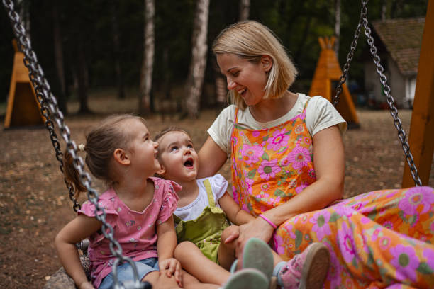 istock Mother joyfully playing on a swing with her twin daughters in a forest playground during a sunny day 2167371430