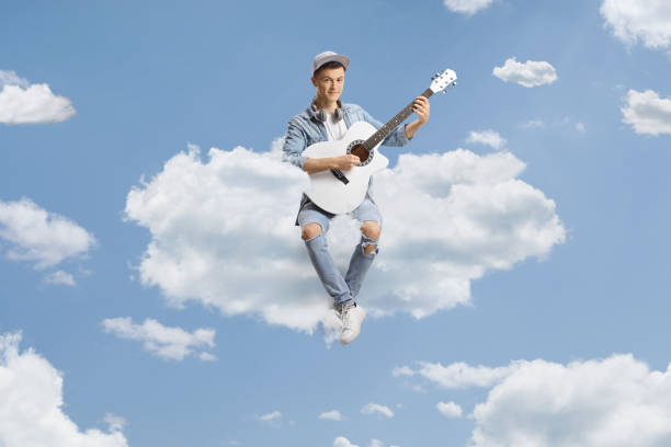 Young man sitting on a cloud and playing an acoustic guitar up in the sky