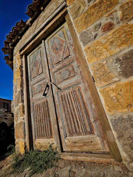 A perspective vertical shot of an old stone house building with double wooden door wings. There are antique designs carved on the surface of the Doors.