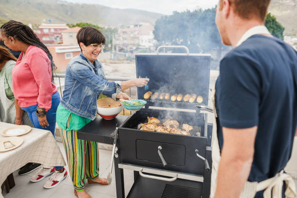 istock Happy friends cooking corncobs and chicken at barbecue rooftop dinner - Multigenerational people having fun during summer time eating and laughing together - Main focus on caucasian woman face 2167381218