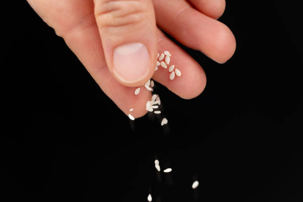 istock Hand pouring white sesame seeds on black background 2167388681