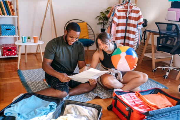 istock Young multiracial couple preparing for leaving on vacation packing suitcases and looking for a place to visit on map 2167393049
