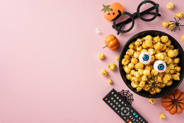 istock Halloween themed popcorn bowl with candy eyeballs, remote control, and other spooky decorations on a pink background 2167406176