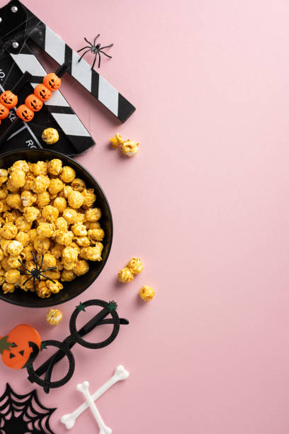 istock Halloween-themed vertical movie night setup with popcorn, spooky decor, clapperboard, and pumpkin ornaments on a pink background 2167406198