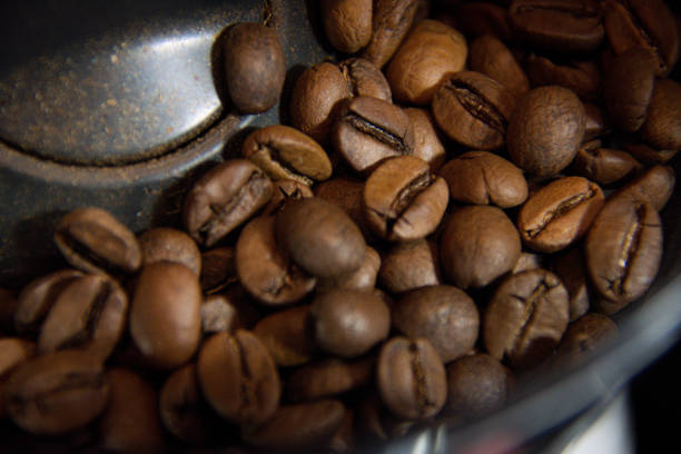 Capture the essence of fresh coffee with this image of roasted coffee beans inside a grinder, ready to be transformed into a delicious brew. The close-up shot highlights the texture and quality of the beans, making it ideal for use in coffee-related marketing, cafe promotions, or barista training materials