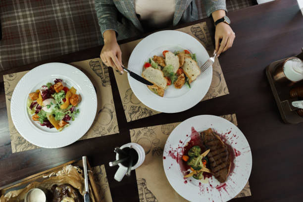 istock Woman sits at a dinner table with Caesar salad, vegetable salad with poached egg and grilled steak Striploin in wine sauce. View from above. Delicious healthy food. 2167411658