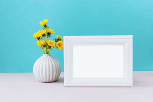 istock White frame mockup with wild yellow dandelion flowers in vase. Empty frame mock up for presentation design. Template 2167411822