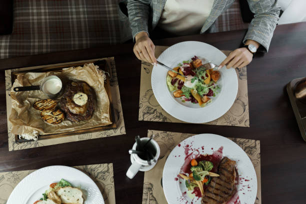 istock Set of dishes from: fried meat with eggplants, vegetable salad with poached egg and steak Striploin in wine sauce. A woman sits at a wooden table holding a fork and knife. Lunch break 2167412240
