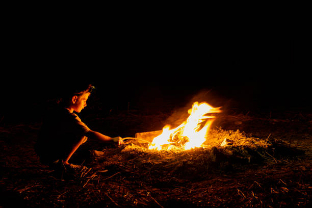 Campfire. a child with a headlamp on his head, illuminated by the fire at night, plays with a stick.