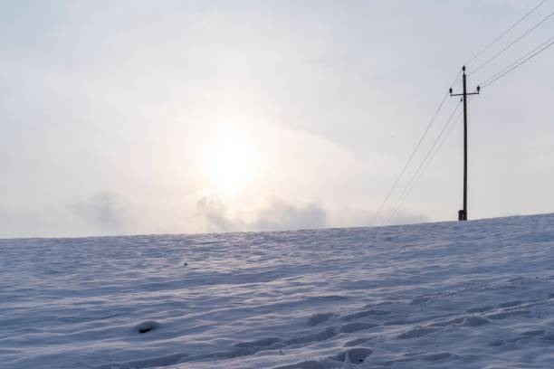 A snowy landscape with a power pole under a cloudy sky during sunset. Bad Schallerbach, Austria
