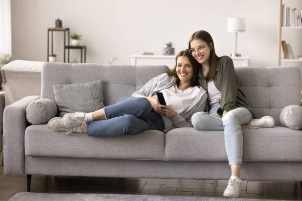 Happy daughter spends weekend time with mother watching television Cheerful middle-aged woman relaxing on sofa with teenager daughter, spend leisure time at home, hold remote controller, selects TV show, watch comedy movie series, enjoy lazy family weekend leisure free girl download stock pictures, royalty-free photos & images