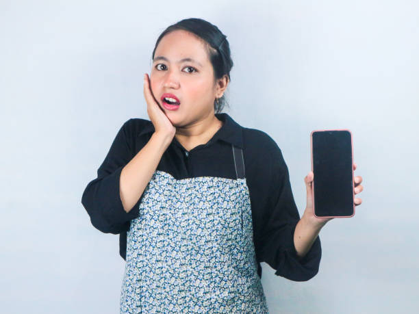istock Surprised expression Asian waitress hold mobile phone with blank empty screen mock up copy space 2167427056
