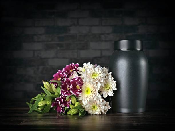 Funeral mourning urn next to a flower bouquet on dark background.