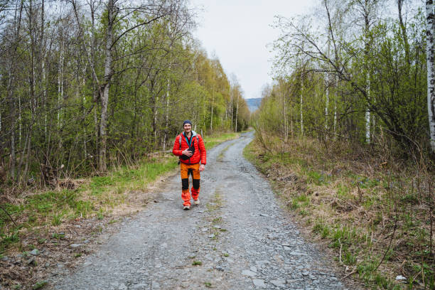 A man strolling along a dirt path through a wooded natural landscape A person is strolling along a forest path surrounded by trees and grass, under the vast sky. The road surface is made of dirt, blending into the natural landscape top view on people walking and cyclists riding stock pictures, royalty-free photos & images