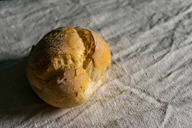 A traditional Alentejano paposeco bread sits on a white tablecloth, capturing the simplicity of Portuguese cuisine. The rustic bread contrasts beautifully with the clean, white setting.