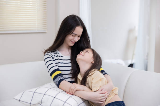 istock Two sisters hug each other with love on the couch 2167438335