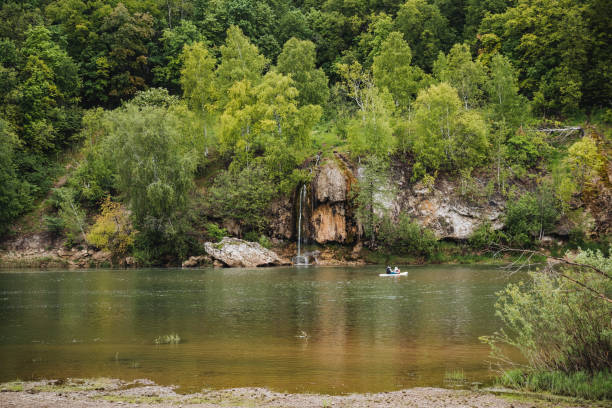 istock In a tranquil setting, a peaceful river winds its way through a beautiful landscape adorned with trees and rocks, while a boat gracefully cruises along the serene waters 2167443614