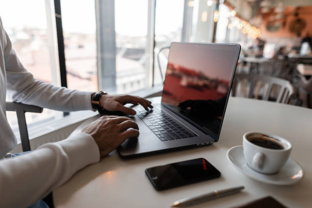 istock Young businessman are sitting at a table in a cafe and typing text on a modern computer. Laptop, coffee and smartphone are on the table. Remote work. Close-up. 2167449029