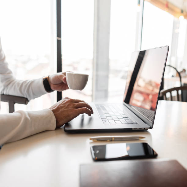 istock Successful man working on a laptop and drinking coffee while sitting in a modern office. Computer and smartphone on the desktop. Side view. 2167449058