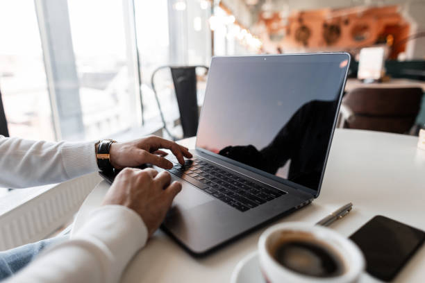 istock Man in a white shirt works at a computer while sitting at a table in a cafe. Successful business man typing on a laptop and drinking coffee. Close-up of man hands. 2167450130