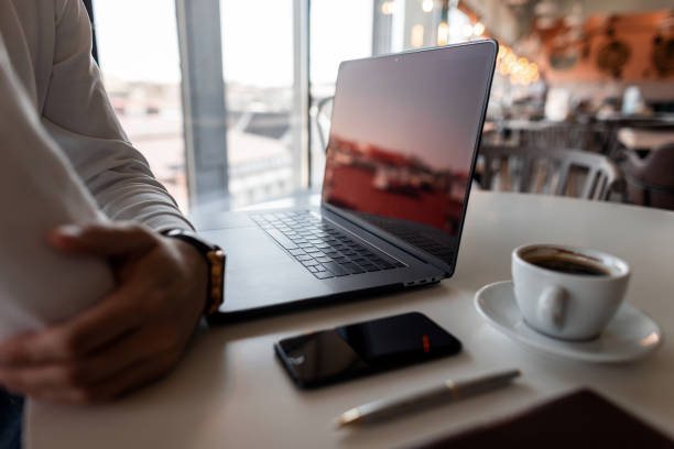 Professional freelancer man is resting sitting at a table in the office with a modern laptop with a cup of coffee from a mobile phone with a brown notebook. Businessman thinks about work.