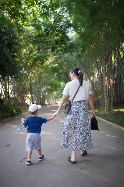 A mother and her young son walk hand in hand down a tranquil path lined with tall trees, enjoying a peaceful moment in nature during a sunny day. China travel scene