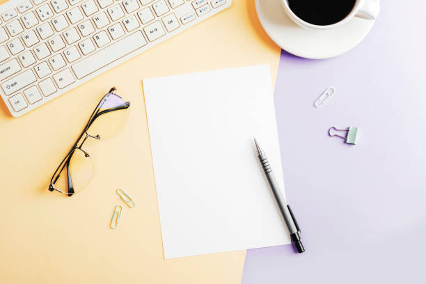 istock Desktop with blank paper, computer keyboard, glasses and coffee cup on beige and purple two-colored background. Top view, flat lay, mockup 2167461873