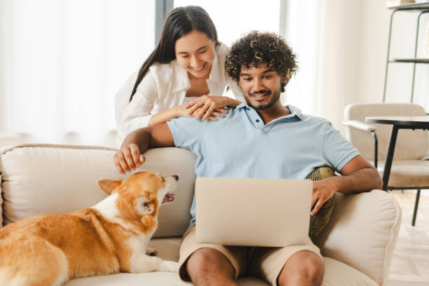 istock Happy couple relaxing on sofa with dog using laptop at home 2167466889