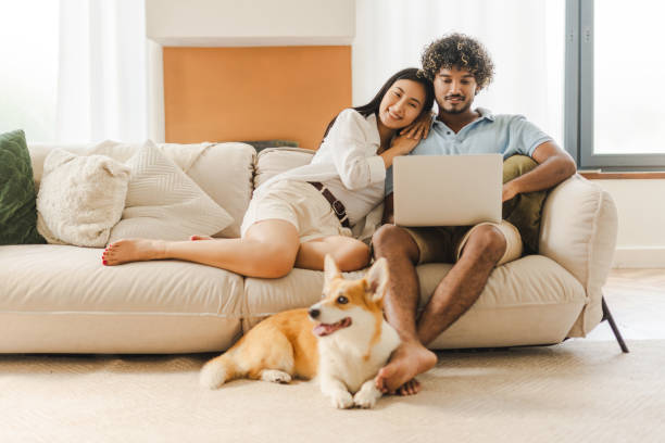 istock Happy multiethnic couple relaxing on sofa with dog and using laptop 2167466891