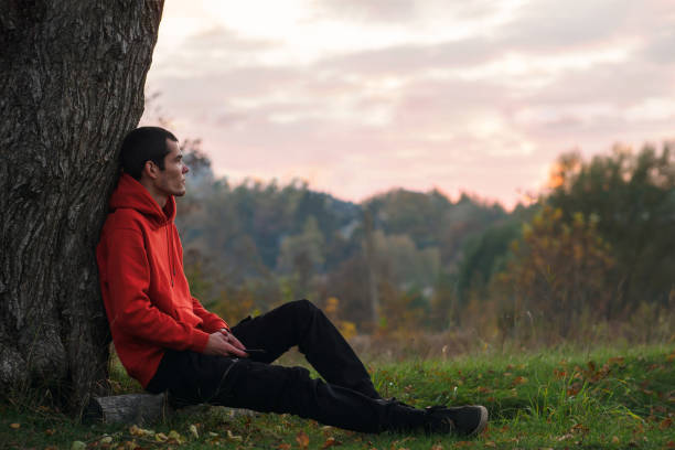 istock A young man is sitting by a tree. Enjoys being alone . Autumn nature. 2167467369