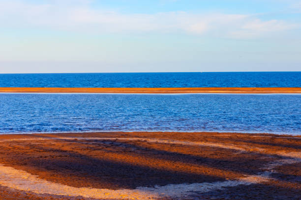 Coast with a body of water in the background. The water is blue and the sand is brown. Beautiful Ocean Coast with  View of islet in the Water
