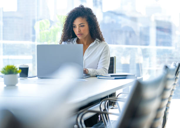 istock Young woman working on a laptop computer in the office. She is sitting at a conference table in a meeting room. 2167470851