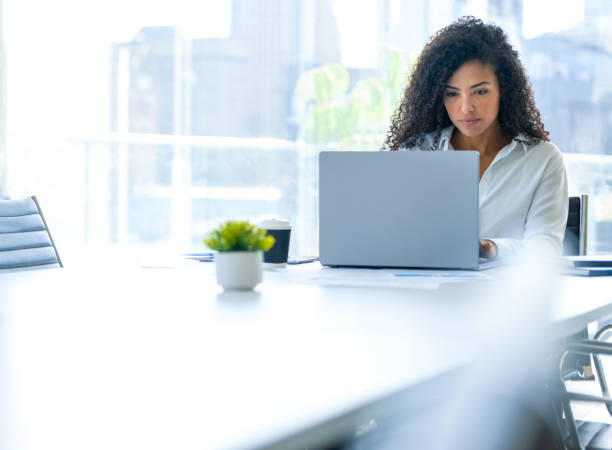 Young woman working on a laptop computer in the office. She is sitting at a conference table in a meeting room.